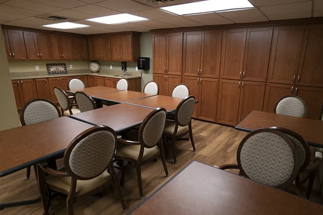 A conference room with wooden tables and upholstered chairs, featuring ample cabinet storage and fluorescent lighting.