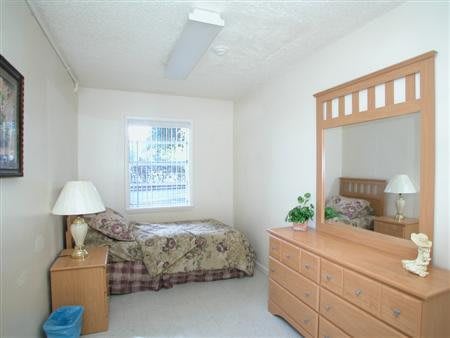 A minimalist bedroom with a single bed, dresser with mirror, and a lamp.