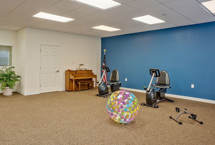 A multipurpose exercise room with stationary bikes, an exercise ball, and a piano against a blue accent wall.