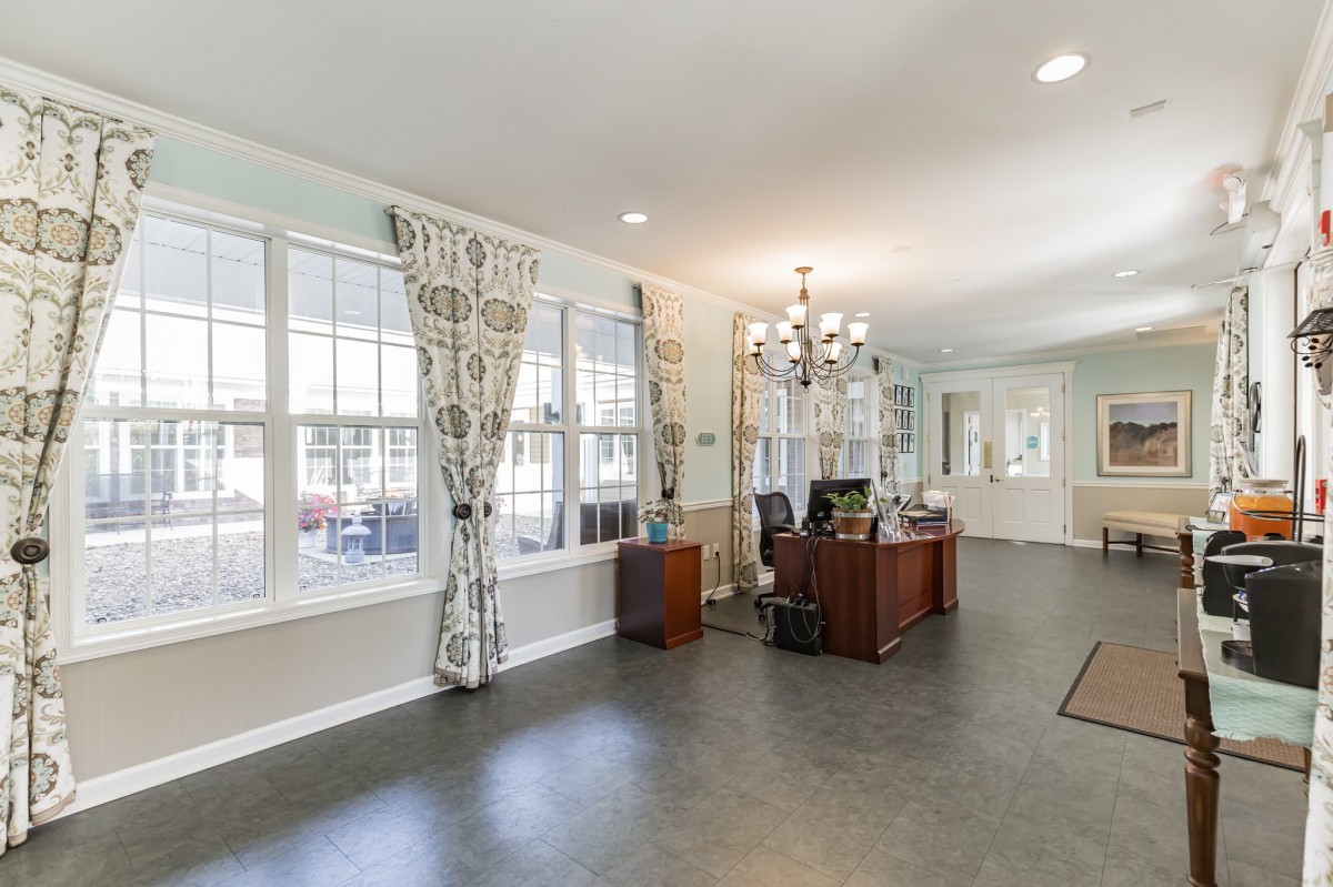 A spacious office interior with a desk, chandelier, and large windows.