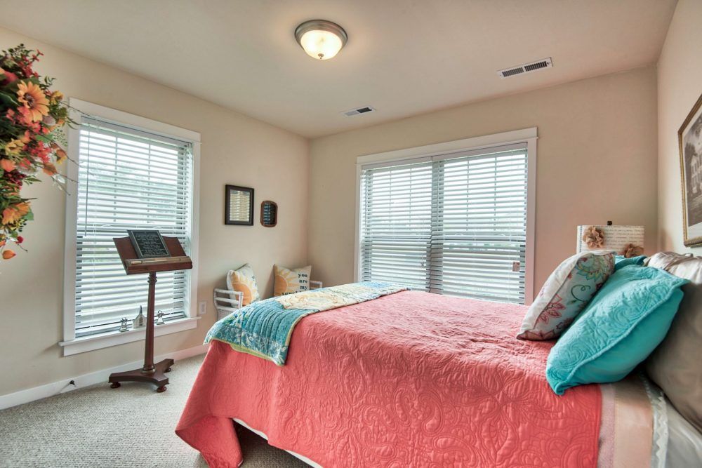 A cozy bedroom with a colorful bedspread and ample natural light coming through the windows.