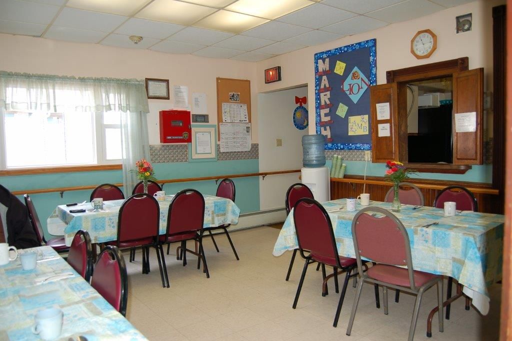 A community dining room with tables and chairs, featuring decorated walls.