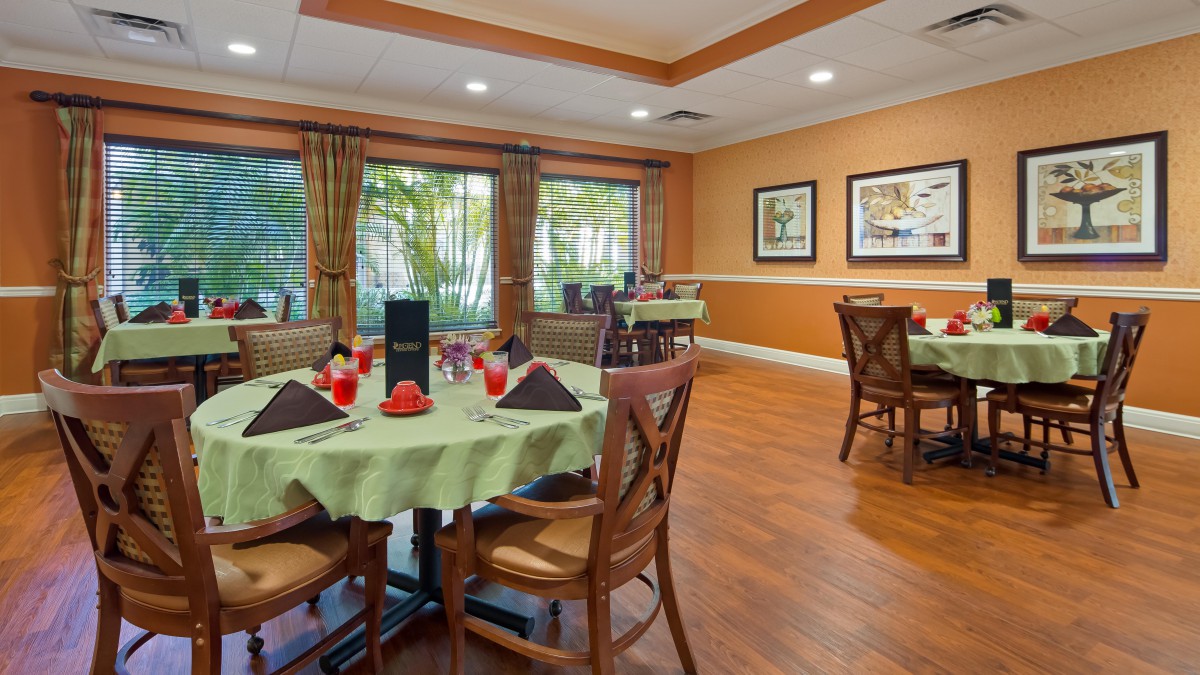 A well-decorated dining area with neatly arranged tables and chairs, featuring large windows and warm lighting.