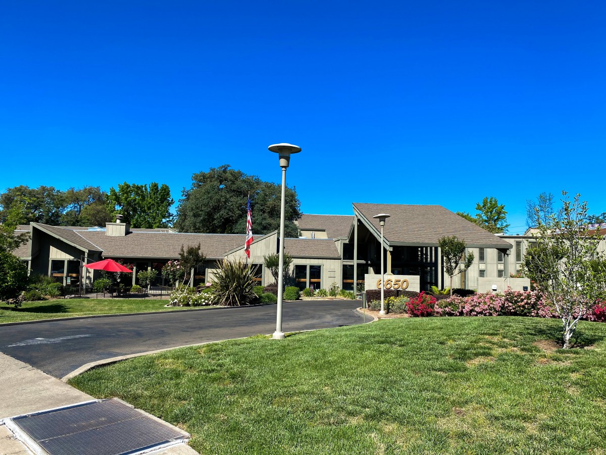 A sunny day view of a building with green grass and a lamp post in the foreground.