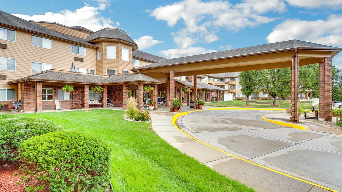 A modern building with an extended canopy over a driveway, surrounded by well-maintained landscaping.