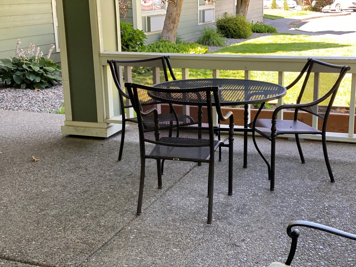A peaceful porch with a set of outdoor chairs and table overlooking a garden.
