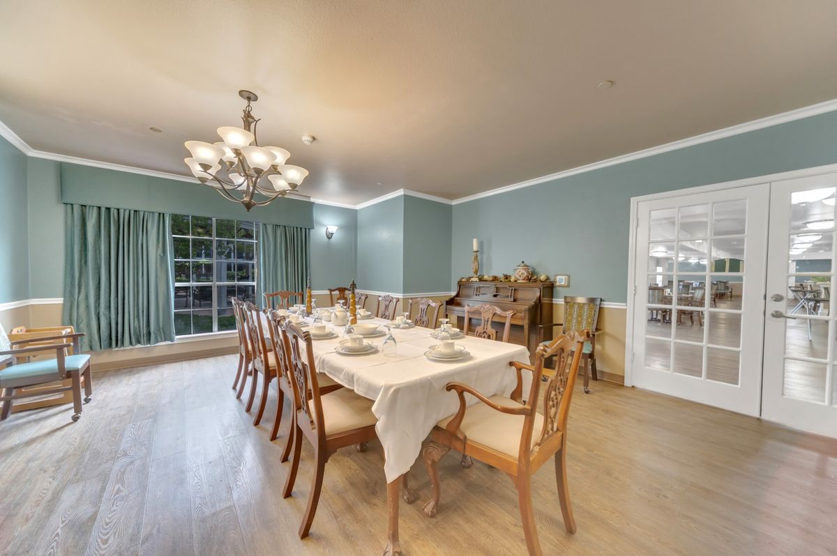 A spacious dining room with a set table, elegant chandelier, and wooden furniture.