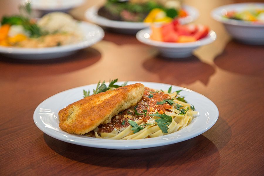 A plate of pasta topped with chicken and garnished with parsley, surrounded by other dishes.