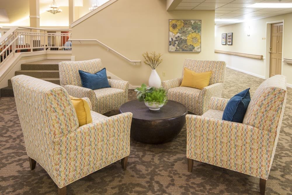 A cozy seating area in a lobby with four patterned chairs, colorful cushions, and a central table adorned with a plant.