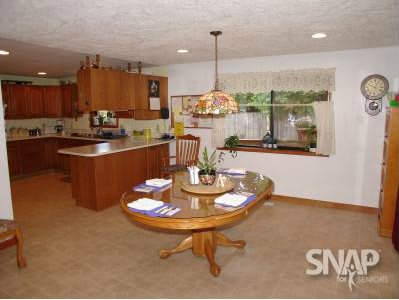 A spacious kitchen and dining area with wooden cabinets and a central table beneath a decorative hanging lamp.