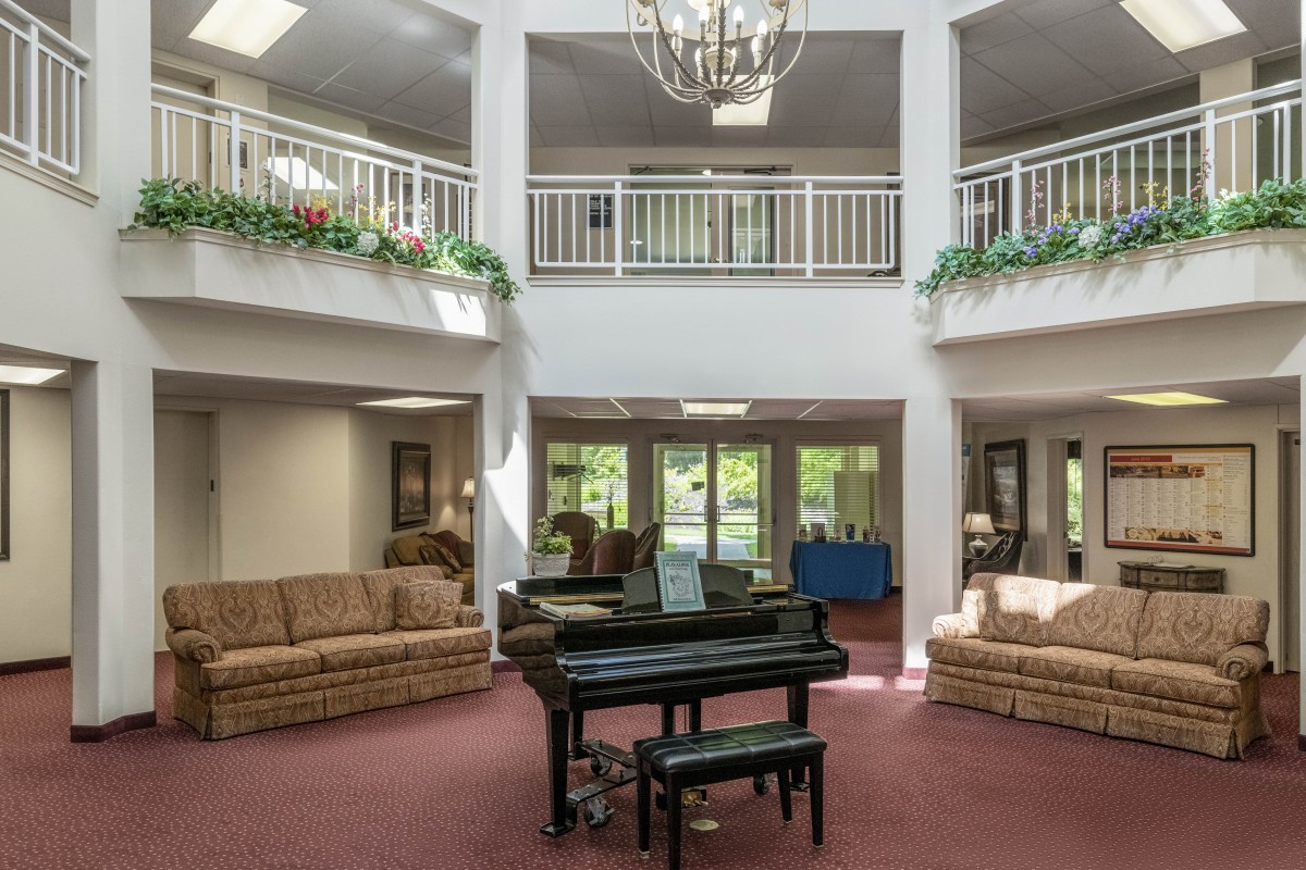 A spacious lobby featuring a grand piano, comfortable sofas, and a chandelier, with natural light streaming in.
