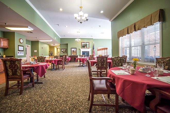 An elegant dining room with neatly arranged tables and chairs, decorated with red tablecloths and a central chandelier.