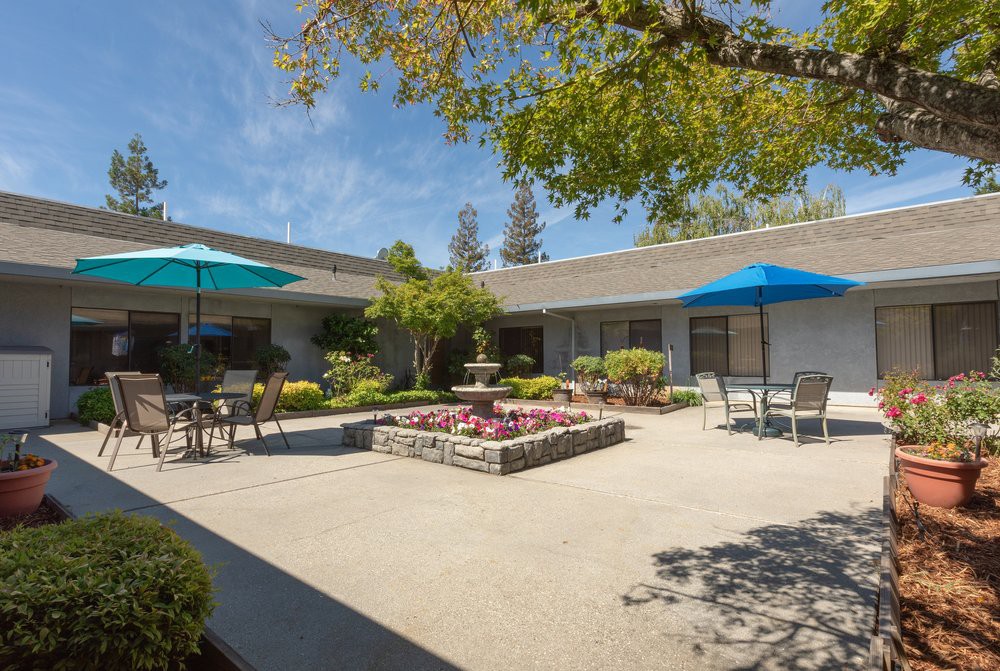 A peaceful courtyard with a central fountain, surrounded by outdoor seating and shaded areas.