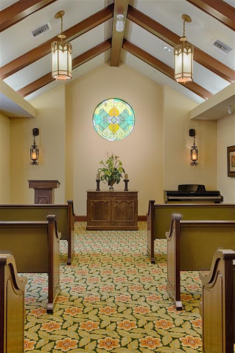 A serene chapel interior featuring wooden pews, a floral arrangement at the altar, and beautiful stained glass.
