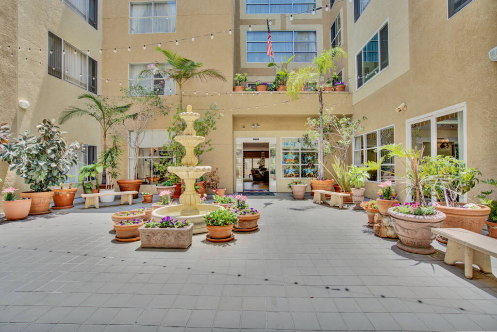 A sunny courtyard with a central fountain surrounded by lush potted plants in an apartment building.