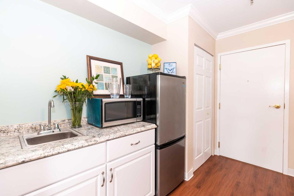 A small kitchenette with a microwave, fridge, and floral decor on the countertop.