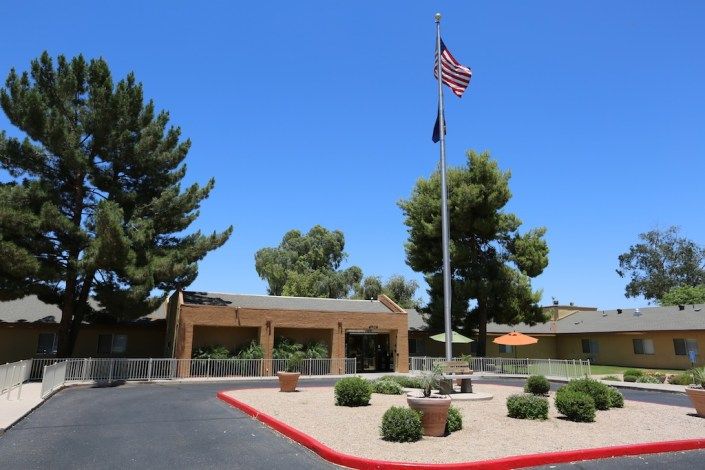 A building entrance with a flagpole displaying the American flag on a sunny day.