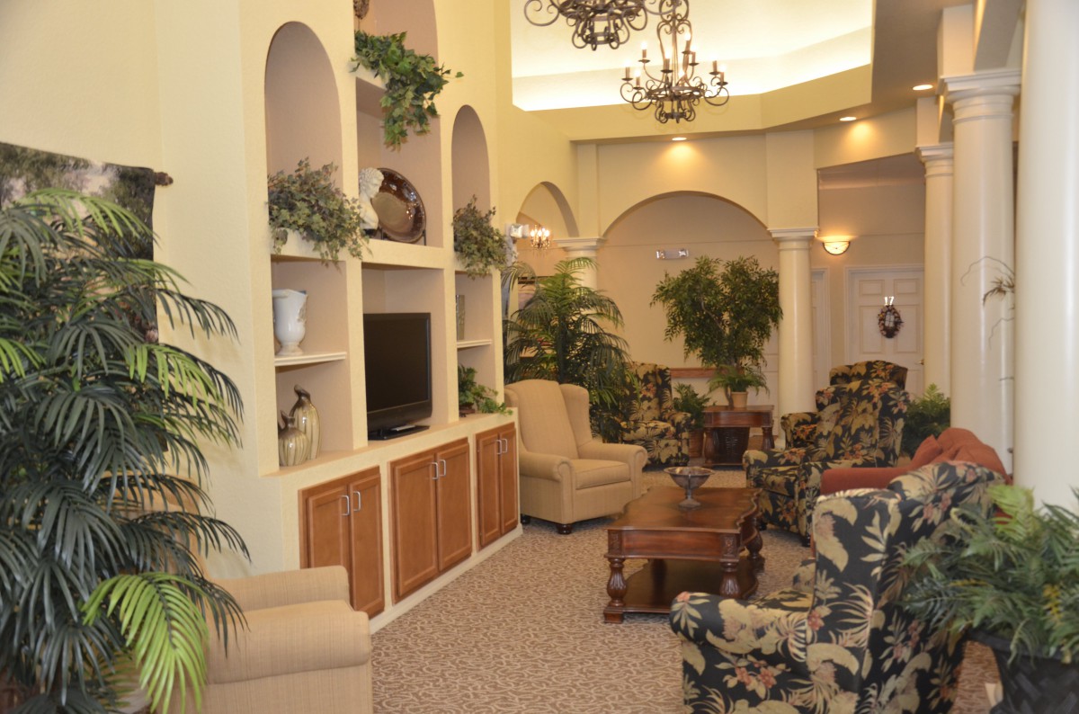 A cozy living room with elegant furniture and greenery, featuring built-in shelves and a television.
