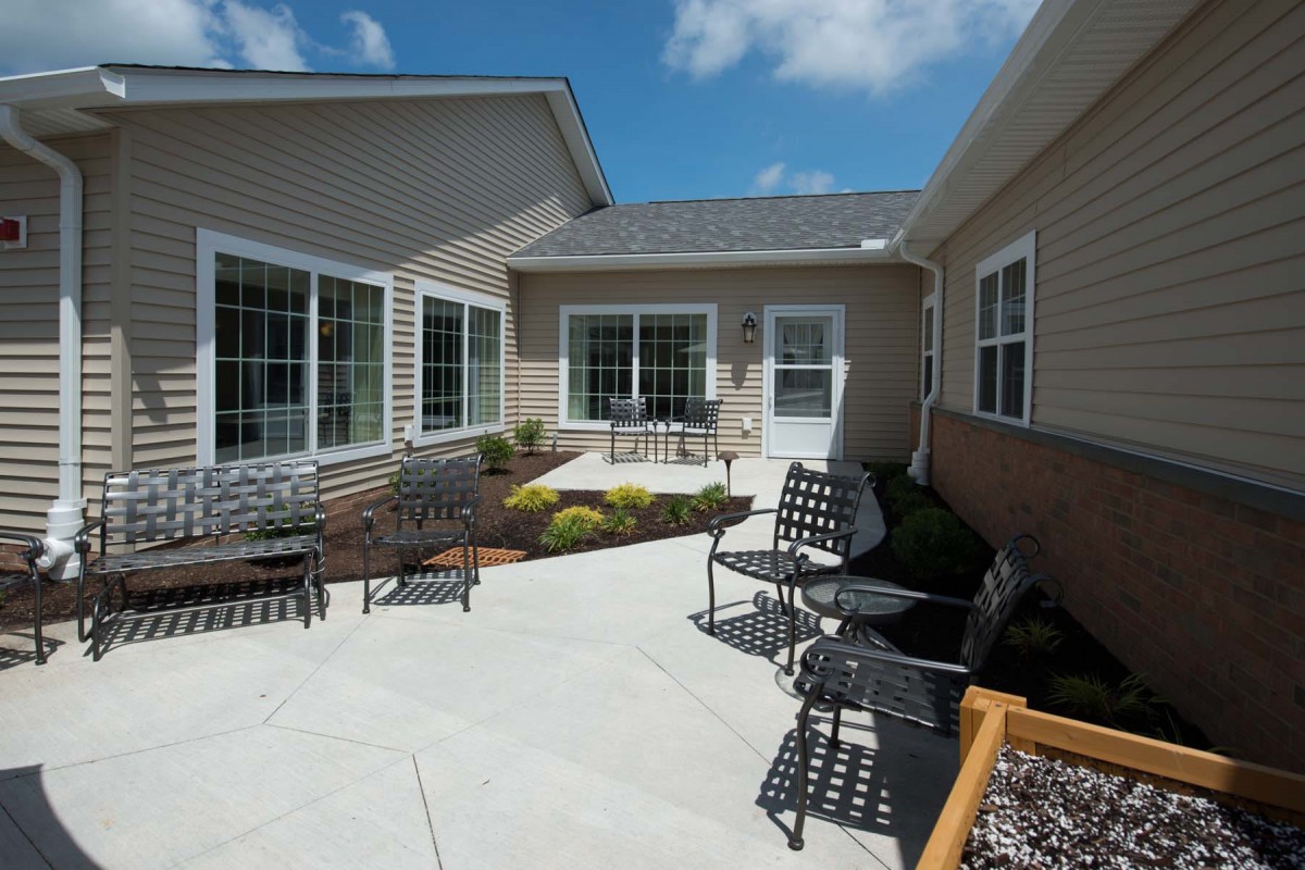 A sunny outdoor patio area with seating and landscaping, surrounded by residential buildings.