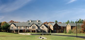 A large estate with a well-maintained lawn and multiple sections to the building, set against a clear blue sky.