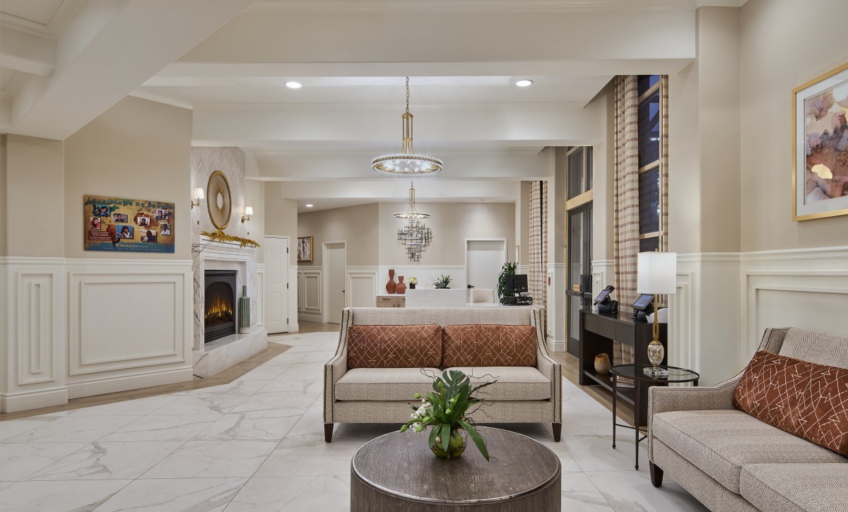 A modern living room with elegant decor, featuring a central sofa, a fireplace, and a chandelier.