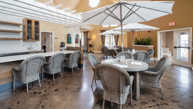 A spacious and elegantly decorated indoor dining area with tables, wicker chairs, and large umbrellas, creating a comfortable and casual atmosphere.