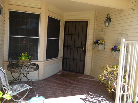 A welcoming front porch with a brick floor, featuring a wrought iron door and decorative plants.