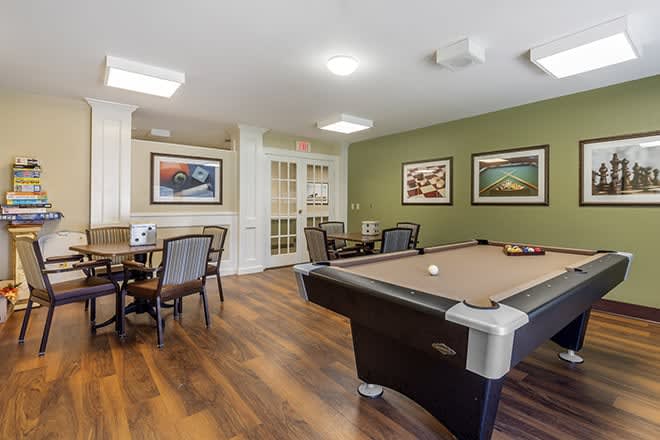 A game room with a pool table, chairs, and tables on a wooden floor.