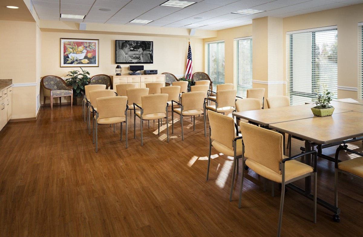 An empty conference room with arranged chairs and tables, a television on the wall, and an American flag in the corner.
