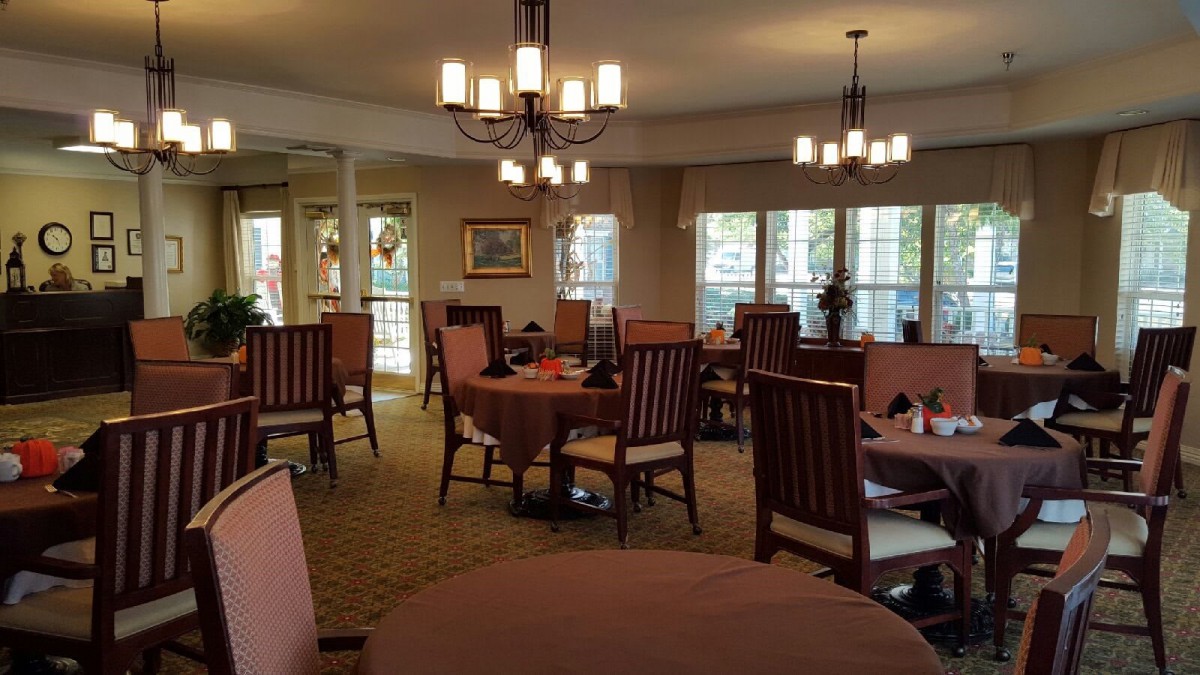 A cozy dining room with neatly arranged tables and chairs, illuminated by elegant chandeliers.