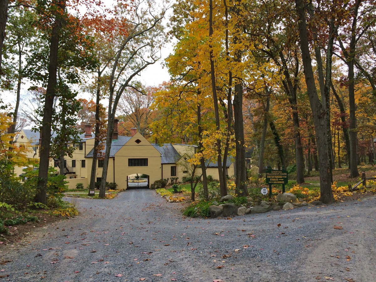 A large house surrounded by autumn trees at the end of a gravel driveway.
