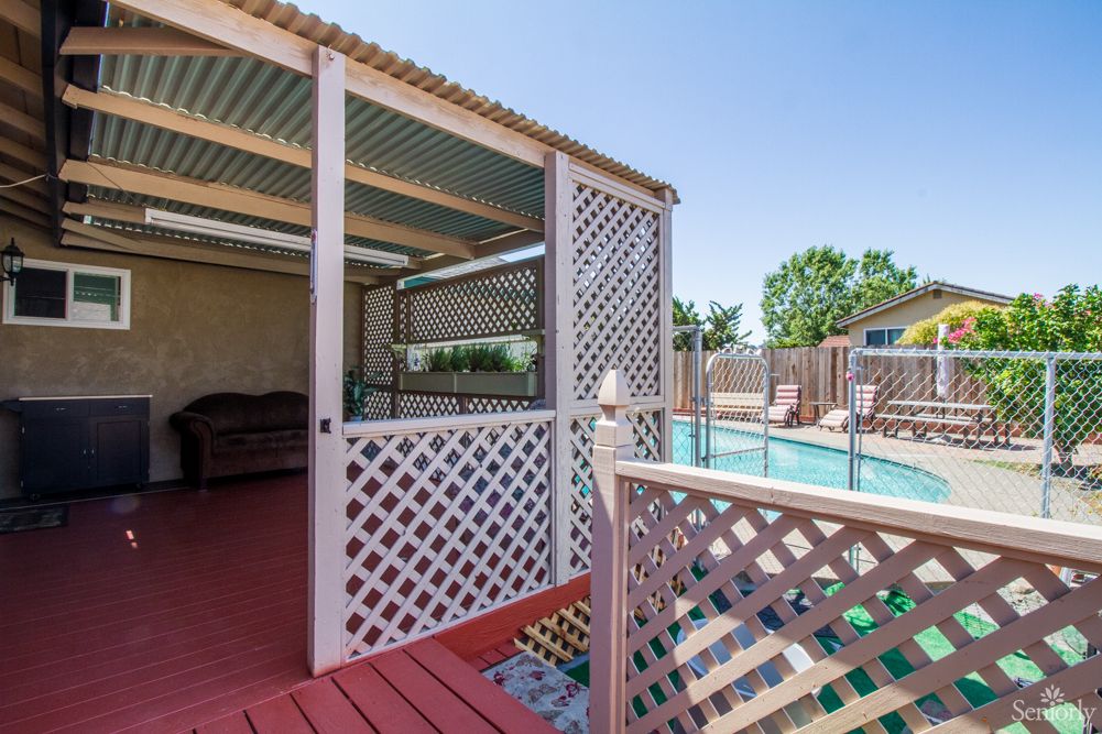 A cozy backyard setup featuring a covered patio with lattice walls and a fenced pool area.