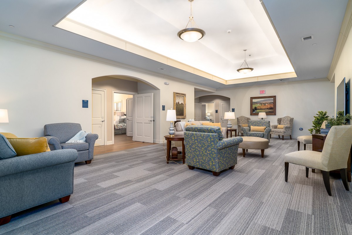A spacious and elegantly designed living area featuring comfortable sofas and chairs, illuminated by ceiling lights.