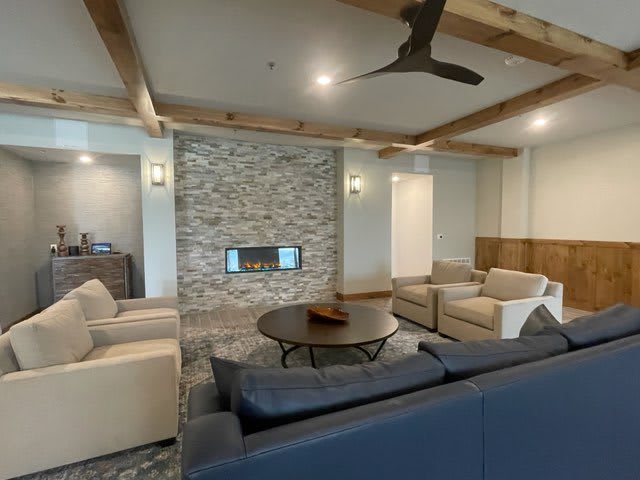 A modern living room featuring a stone fireplace, wooden ceiling beams, and a comfortable seating arrangement.