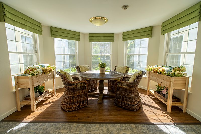 A cozy dining area with wicker chairs and a round table, bathed in natural light from multiple windows.