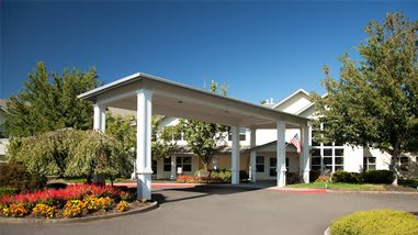 A well-maintained building entrance with a portico, surrounded by landscaped gardens on a sunny day.
