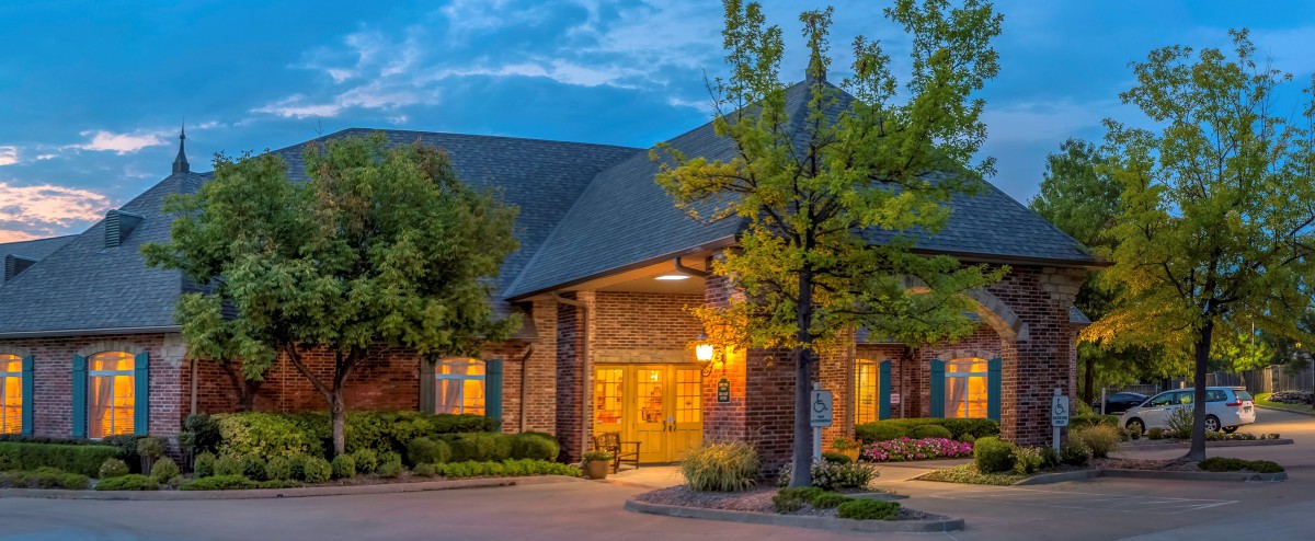 A warmly lit brick building surrounded by trees in the evening.