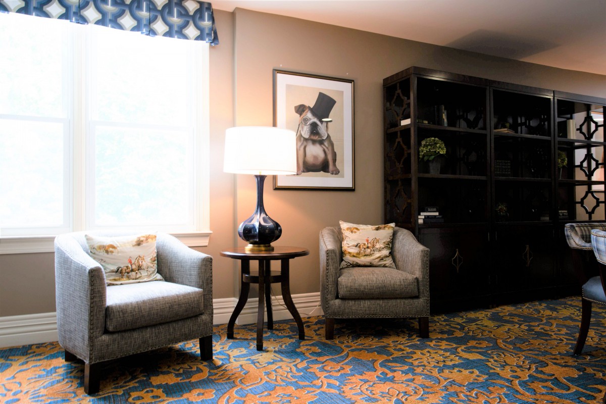 A cozy living room corner with two armchairs, a table lamp, and a decorated bookshelf.