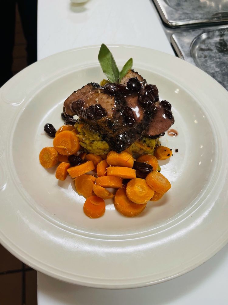 A gourmet dish featuring sliced meat topped with a sauce and garnished with blueberries, served alongside sliced carrots.