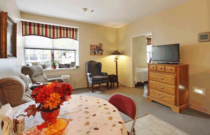 A cozy living room with a mix of comfortable furniture, including an armchair and a TV on a dresser.