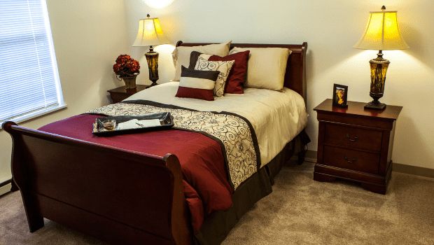 A cozy bedroom with a neatly made bed, decorative pillows, and a bedside lamp.