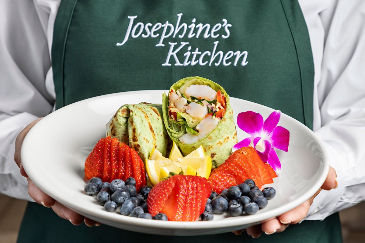 A healthy wrap served with fresh strawberries, blueberries, and a decorative flower at Josephine's Kitchen.