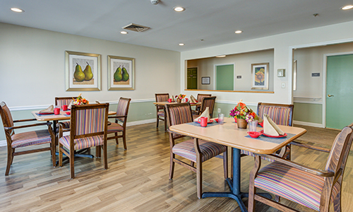 A cozy dining room with neatly arranged tables and chairs, featuring decorative wall art and a warm wooden floor.