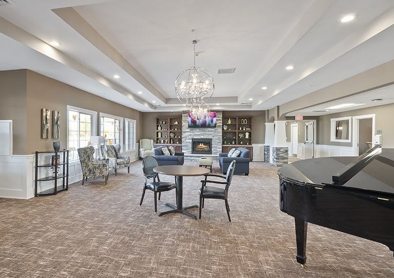 A spacious and elegantly decorated living room featuring a grand piano, chandelier, and comfortable seating around a fireplace.