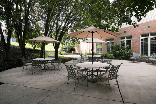 A serene outdoor patio area featuring tables and seating under large umbrellas, surrounded by lush greenery.