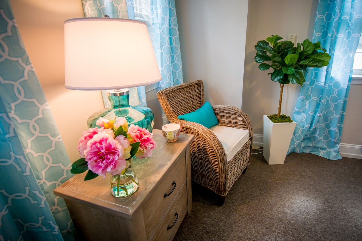 A cozy living room corner with a wicker chair, side table, and vibrant floral arrangement under soft lighting.