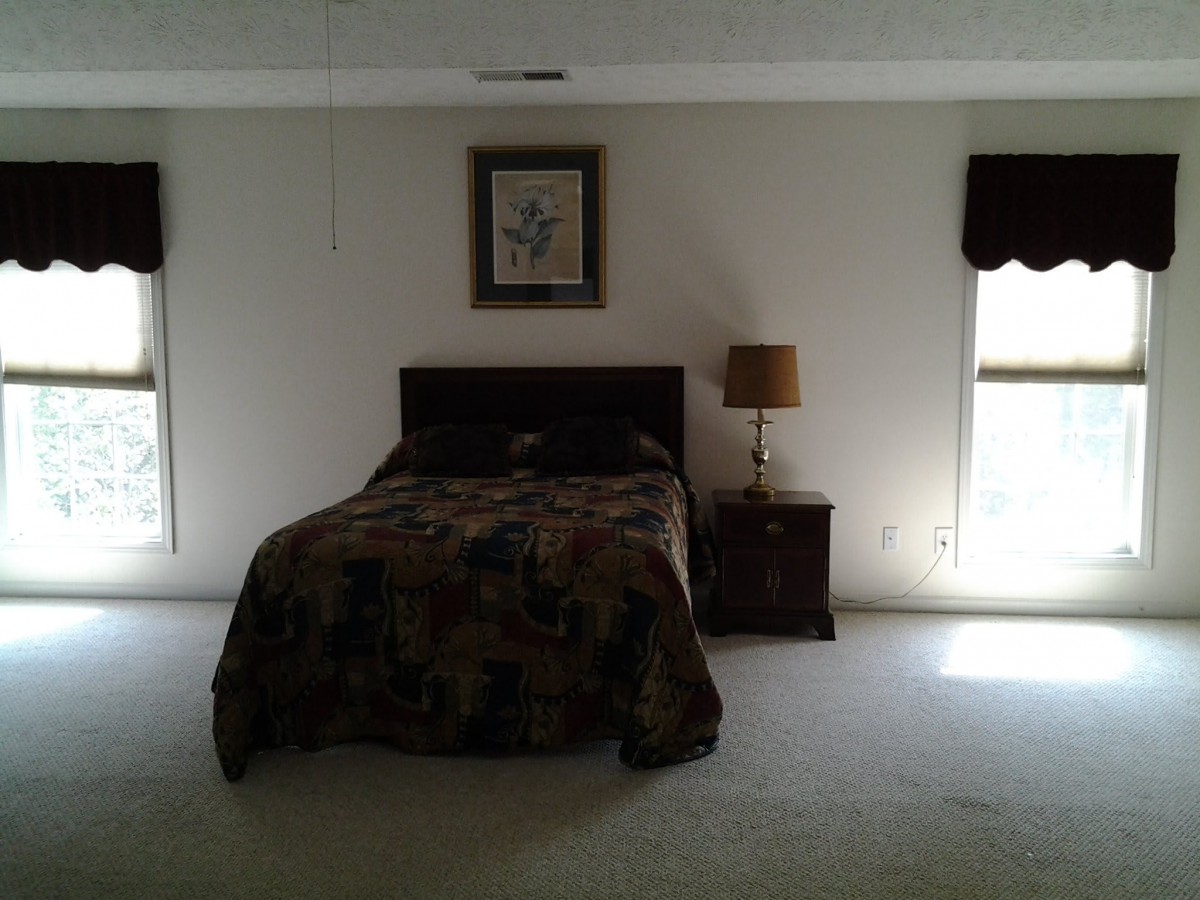 A simple bedroom with a bed, nightstand, and lamp between two windows.