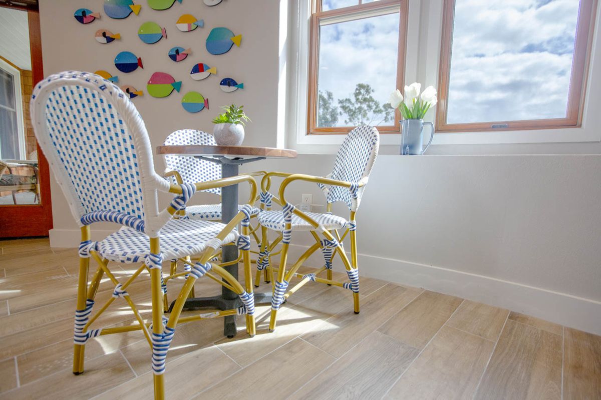 A sunlit cafe interior with woven chairs, a round table, and vibrant wall decor.