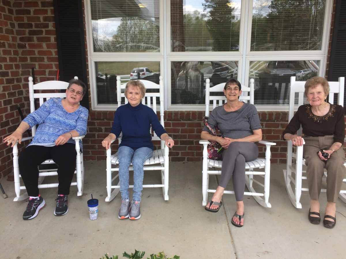 A group of people sitting on white rocking chairs on a porch.