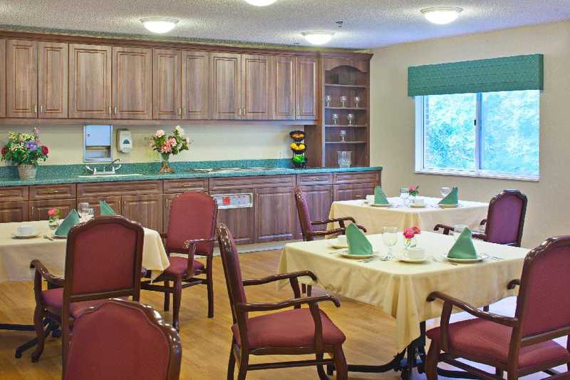 A neatly arranged dining area with tables, chairs, and a kitchenette in the background.